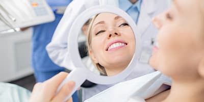 Reflection in mirror of healthy smile of pretty young smiling female patient