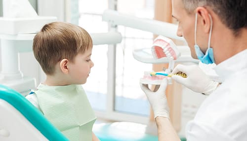 Dentist educating little boy about brushing teeth in clinic