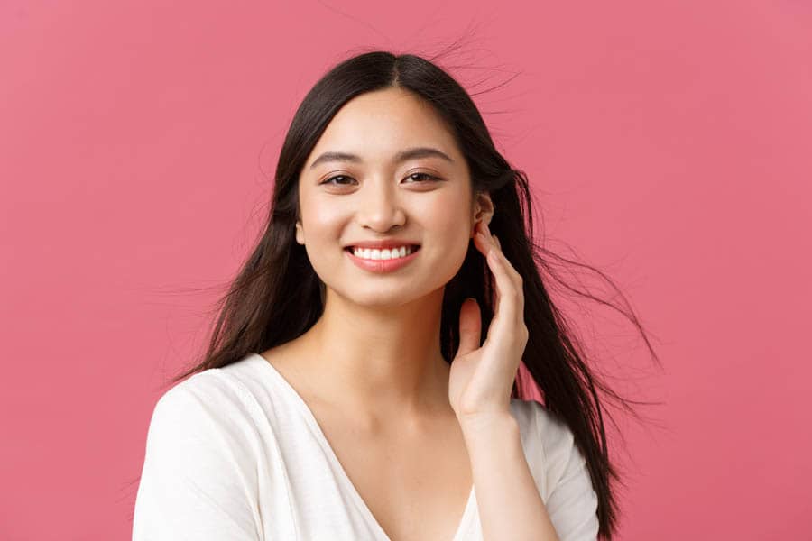 Beauty salon, haircare and skincare products advertisement concept. Close-up of beautiful young asian woman smiling as wind softly blowing at haircut, standing pink background