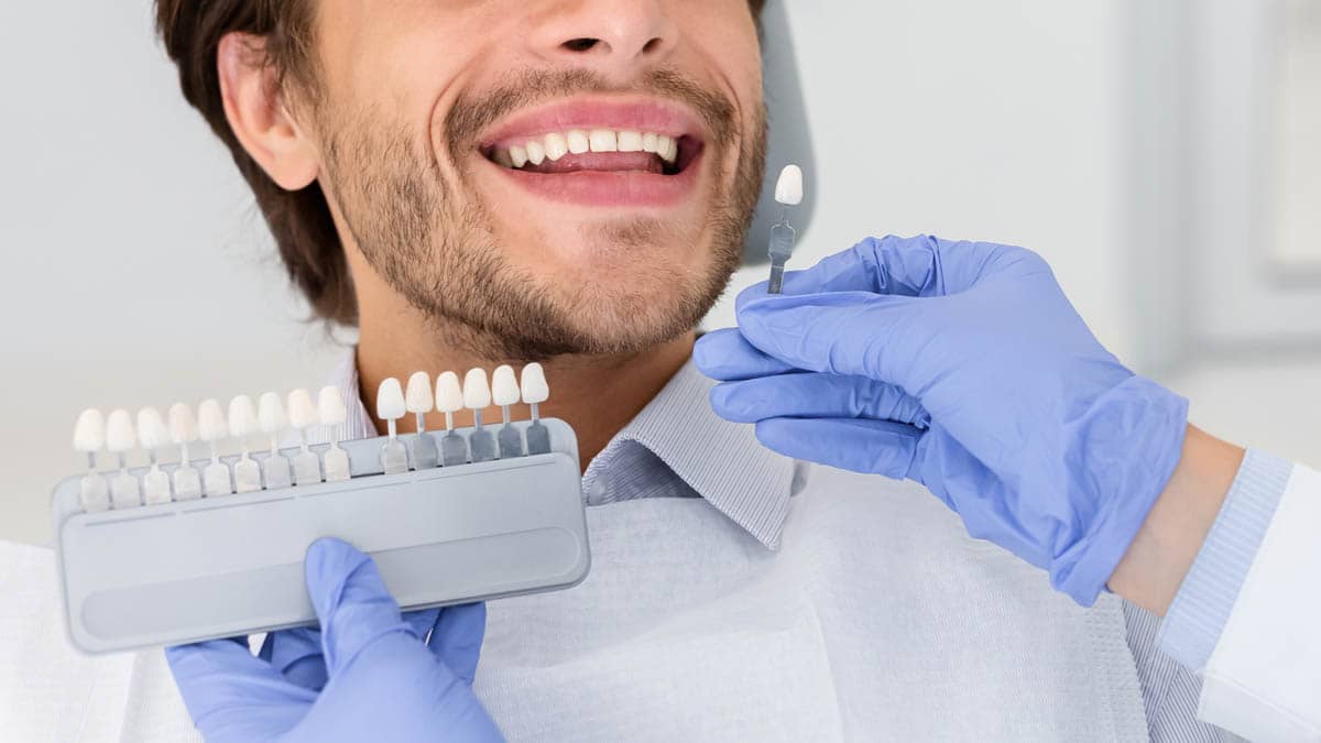 Dentist applying sample from tooth scale to smiling man teeth
